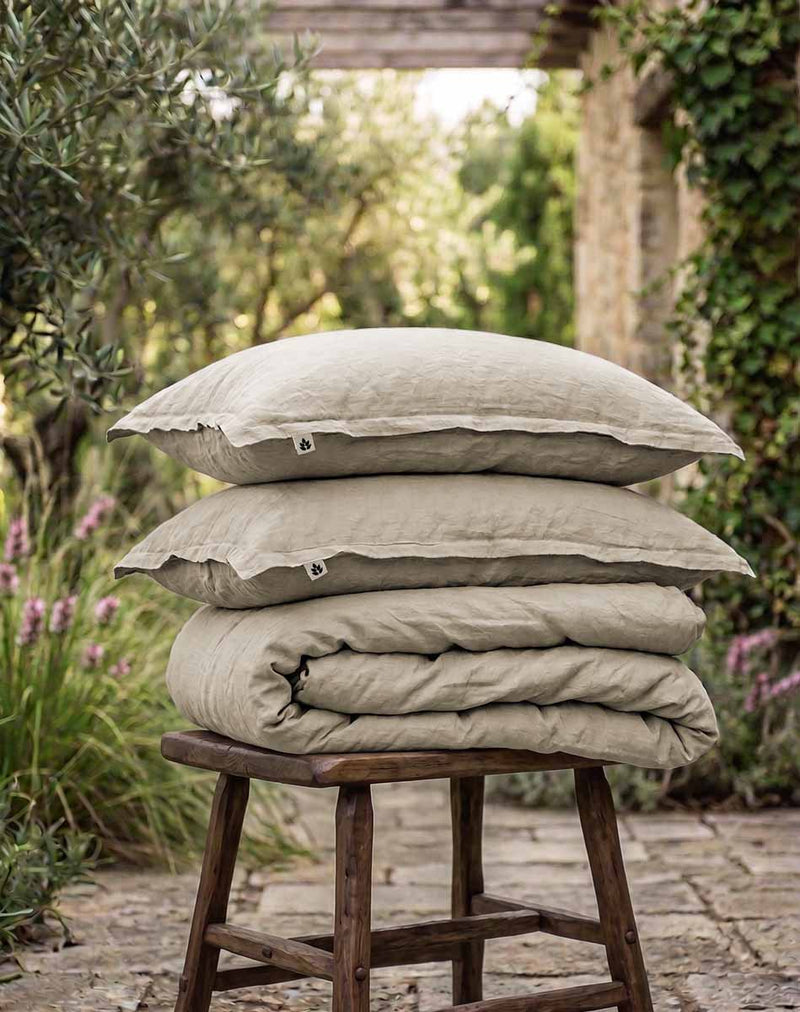 Linen pillow cases and duvet cover with Ada & Ina Labels on a rustic wooden stool.